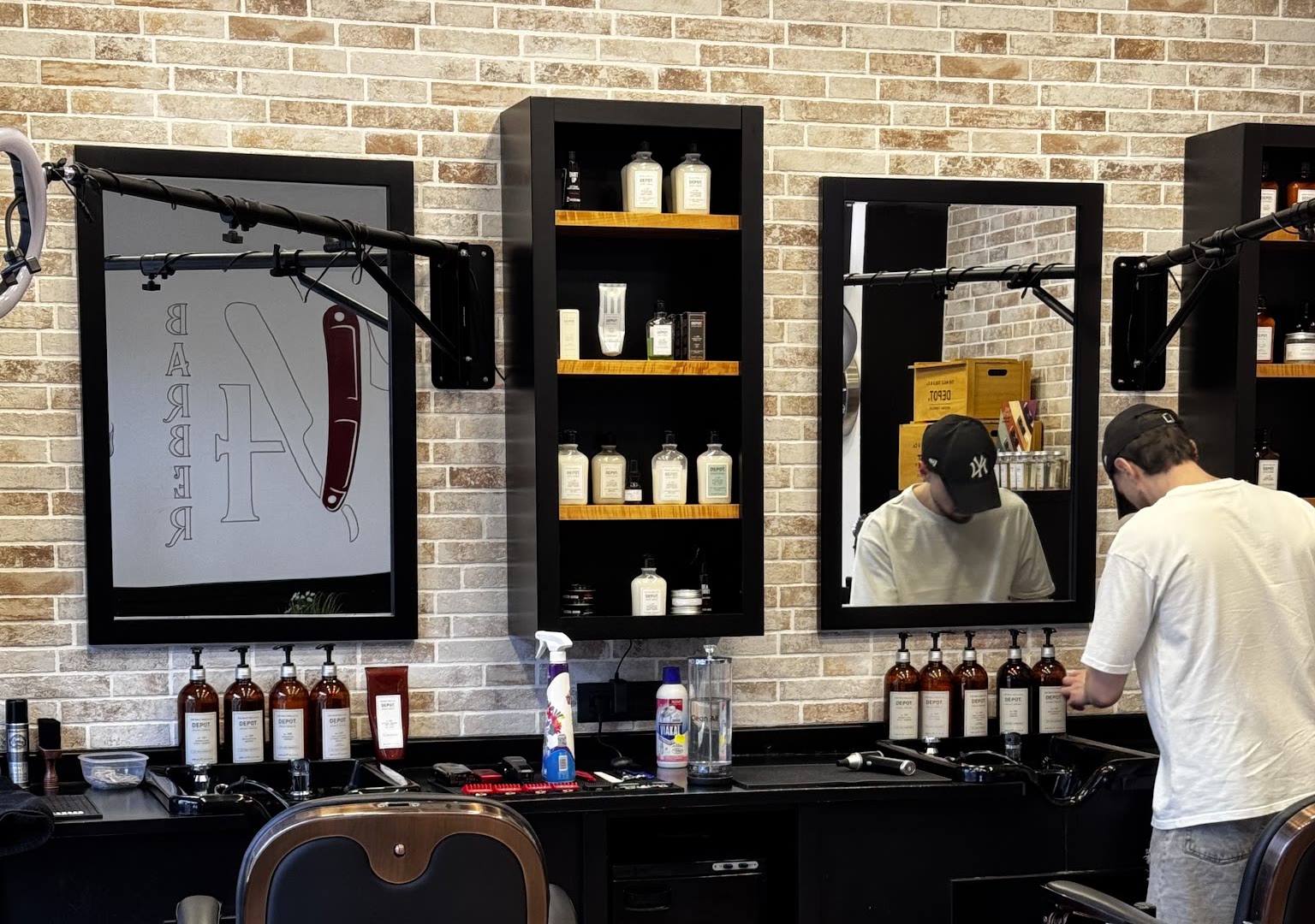 La sala coi mattoni bianchi: gli specchi neri col logo 14 Barber, le mensole coi prodotti e le postazioni